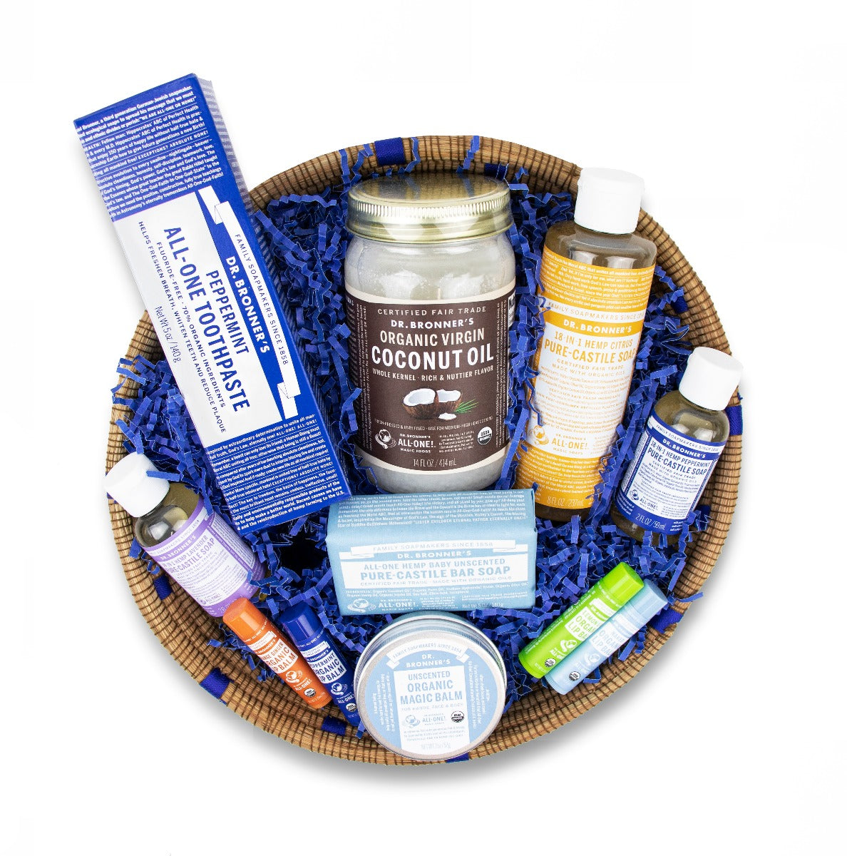 A basket contains various Dr. Bronners products, including organic virgin coconut oil, peppermint toothpaste, liquid Castile soaps, bar soap, and lip balms, nestled in blue decorative paper, ideal for eco friendly gift ideas