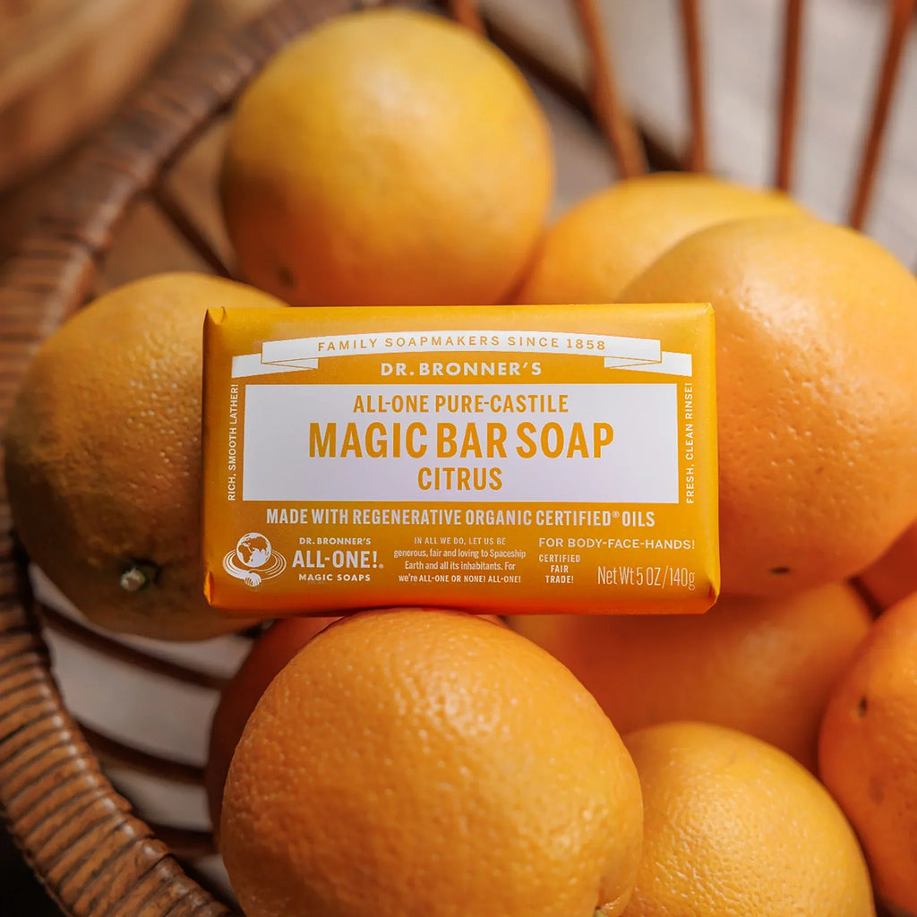 A bar of Dr. Bronners Magic Bar Soap Citrus rests among oranges in a wooden basket. The vibrant soap packaging contrasts with the natural backdrop, highlighting organic ingredients and eco friendly ethos. Dr. Bronners All One Magic Bar Soap Citrus, Made with Organic Oils [5 oz]