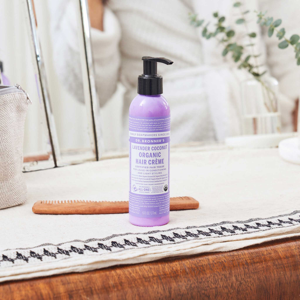 A bottle of Dr. Bronners lavender soap stands on a bathroom countertop, surrounded by a hand towel, mirror, and eucalyptus plant. The setting suggests a serene, eco friendly environment [6 oz]